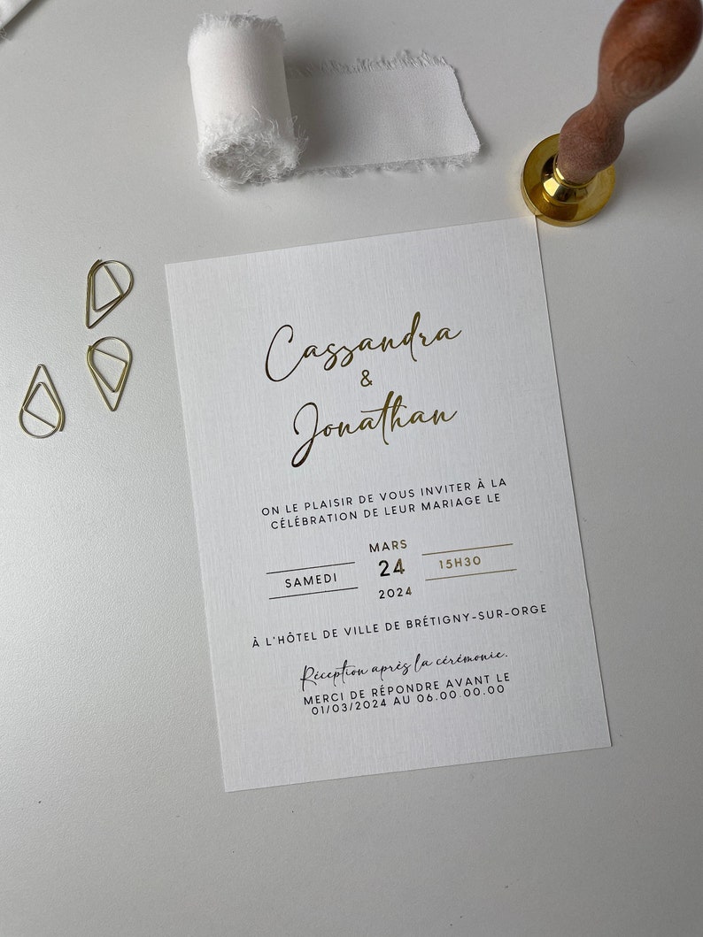 Puede incluir: Una invitaci&oacute;n de boda blanca con letras doradas anunciando el matrimonio de Cassandra y Jonathan. La boda tendr&aacute; lugar el s&aacute;bado 24 de marzo de 2024 a las 3:30 PM en el Hotel de Ville de Br&eacute;tigny-sur-Orge. La recepci&oacute;n tendr&aacute; lugar despu&eacute;s de la ceremonia. Por favor, responde antes del 1 de marzo de 2024.
