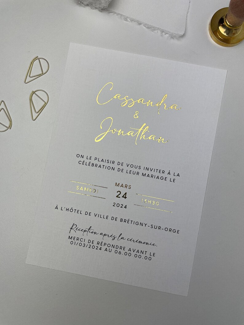 Puede incluir: Una invitaci&oacute;n de boda con letras doradas que anuncian el matrimonio de Cassandra y Jonathan el s&aacute;bado 24 de marzo de 2024 a las 15:30 en el H&ocirc;tel de Ville de Br&eacute;tigny-sur-Orge. La invitaci&oacute;n incluye una solicitud de respuesta antes del 1 de marzo de 2024.