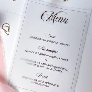 Puede incluir: Un menú de boda con un borde dorado y texto. El menú incluye los siguientes platos: Entree - Tournedos de Filet de Boeuf, Jus Tonka. Plat Principal - Feuilleté de Fourme d'Ambert aux Poires o Filet de Dorade, acompañado de un risotto al parmesano y un tian de verduras. Postre - Wedding Cake Crème Meringuée et Confit de Citron.