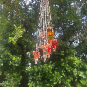 May include: A set of eight crystal point pendulums with silver chains. The pendulums are filled with various colors of crystals, including red, orange, yellow, green, blue, and purple.