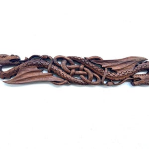 May include: A wooden wall sculpture of two dragons intertwined in a Celtic knot design. The dragons are carved in a dark brown wood and have intricate details.