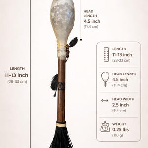 Könnte beinhalten: Eine handgefertigte zeremonielle Rassel mit einem hellfarbigen Kopf, 11,4 cm Kopflänge und 6,4 cm Kopfbreite. Der Holzgriff ist mit Federn und einer schwarzen Quaste verziert. Die Rassel ist 28-33 cm lang und wiegt 110 g.