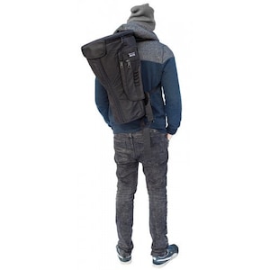 May include: A black instrument case is carried over the shoulder. The case has a rectangular shape with a curved top and a side pocket. The person is wearing a blue and gray hoodie, gray beanie, and gray jeans.