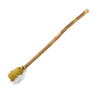 May include: A handcrafted drum beater with a long, natural wood handle. The striking end features a tan suede-like material with white fur trim, creating a soft, textured surface for sound production. The beater is designed for percussion instruments.