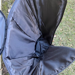 May include: Open black case with a zippered closure, revealing a spacious interior lined with black fabric. The case is designed to hold and protect items, with a focus on functionality and storage.