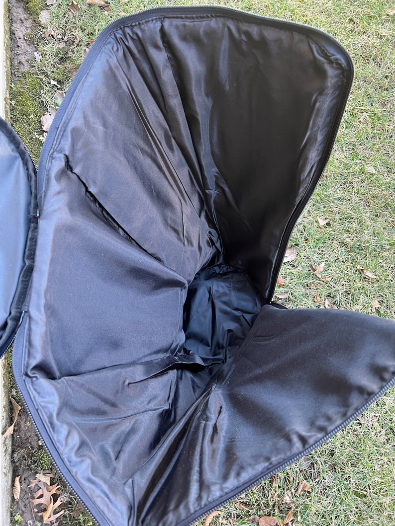 May include: Open black case with a zippered closure, revealing a spacious interior lined with black fabric. The case is designed to hold and protect items, with a focus on functionality and storage.
