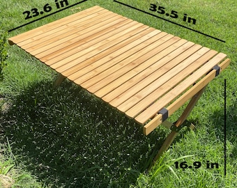 May include: A wooden folding table with a natural finish. The table is 90.2 cm long, 60 cm wide, and 42.9 cm high.