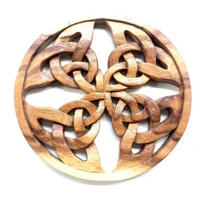 May include: A round wooden wall hanging with a carved Celtic knot design. The knot is intricately woven and has a light brown color.