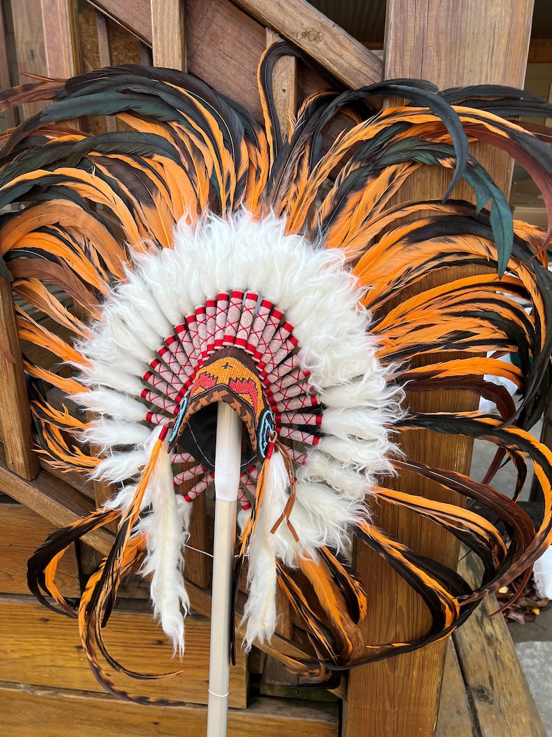May include: A Native American headdress with orange and black feathers, white fur trim, and red and white beaded accents.