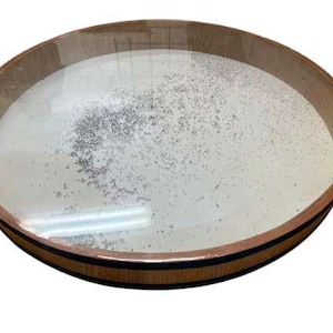 Op de afbeelding: Een ronde houten kom met een lichtgekleurd interieur en een donkerbruine rand. De binnenkant van de kom bevat een lichtgekleurde substantie met kleine, donkere deeltjes. De kom staat tegen een witte achtergrond.