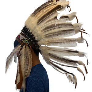 May include: A traditional Native American headdress with white and brown feathers, a leather band, and beaded accents.