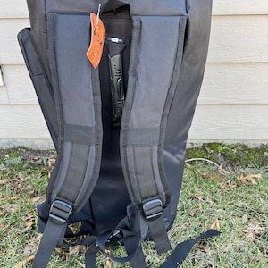 May include: Black backpack with adjustable shoulder straps and a handle. The backpack has a zippered top and a tag hanging from the handle. The backpack is made of a durable material and is designed for carrying items.