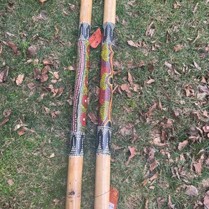 May include: Two wooden percussion sticks with black, red, yellow, and white painted designs. The sticks are approximately 20 inches long.