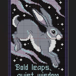 May include: A cross-stitch pattern featuring a grey rabbit leaping against a black background with white stars and light purple wisps. The text "Bold leaps, quiet wisdom" is stitched in light blue at the bottom, all enclosed in a purple border.