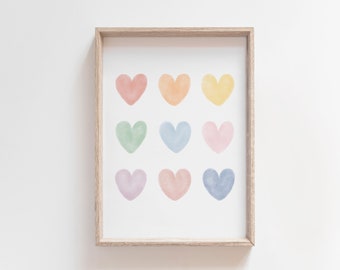Puede incluir: Una impresión enmarcada con nueve corazones de acuarela en un esquema de colores arcoíris. Los corazones están dispuestos en tres filas de tres. El marco es de color madera claro.