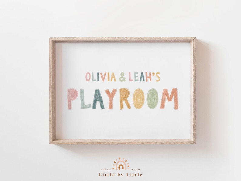 May include: A framed print with the text "Olivia & Leah's Playroom" in colorful, hand-drawn letters. The letters are in shades of pink, orange, yellow, green, and blue.