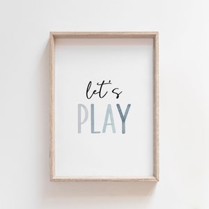 May include: A framed print with the text "let's PLAY" in a blue watercolor gradient. The frame is light wood.