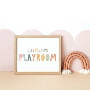 May include: A framed print with the text "ELIZABETH'S PLAYROOM" in colorful, hand-drawn letters. The print is displayed on a shelf with a small, woven rainbow decoration.
