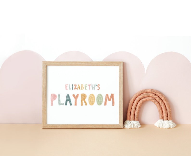 May include: A framed print with the text "ELIZABETH'S PLAYROOM" in colorful, hand-drawn letters. The print is displayed on a shelf with a small, woven rainbow decoration.