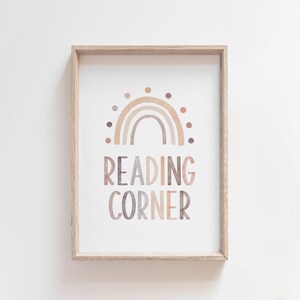 K&ouml;nnte beinhalten: Ein gerahmter Druck mit einem Aquarell-Regenbogen-Design und dem Text "READING CORNER" in einem Farbschema aus Braun, Beige und Lila.