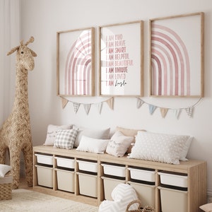 May include: Three framed prints featuring pink watercolour rainbows. The centre print includes the text "I am kind, I am brave, I am smart, I am helpful, I am beautiful, I am unique, I am loved, I am Layla".