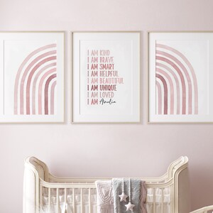 May include: Three framed prints featuring pink watercolour rainbows. The centre print displays the text "I am kind, I am brave, I am smart, I am helpful, I am beautiful, I am unique, I am loved, I am Amelia".
