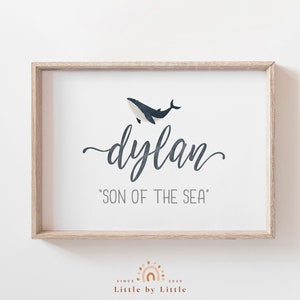 Può includere: Una stampa incorniciata con un'illustrazione di una balena e il testo "dylan 'SON OF THE SEA'" in un carattere grigio chiaro. La cornice è in legno chiaro.