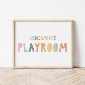 May include: A framed print with the text "Benjamin's Playroom" in colorful, hand-drawn letters. The letters are in shades of pink, orange, yellow, green, and blue.