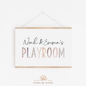 May include: A white sign with a wooden frame hangs on a white wall. The sign says "Noah & Emma's PLAYROOM" in a colorful, watercolor-style font.