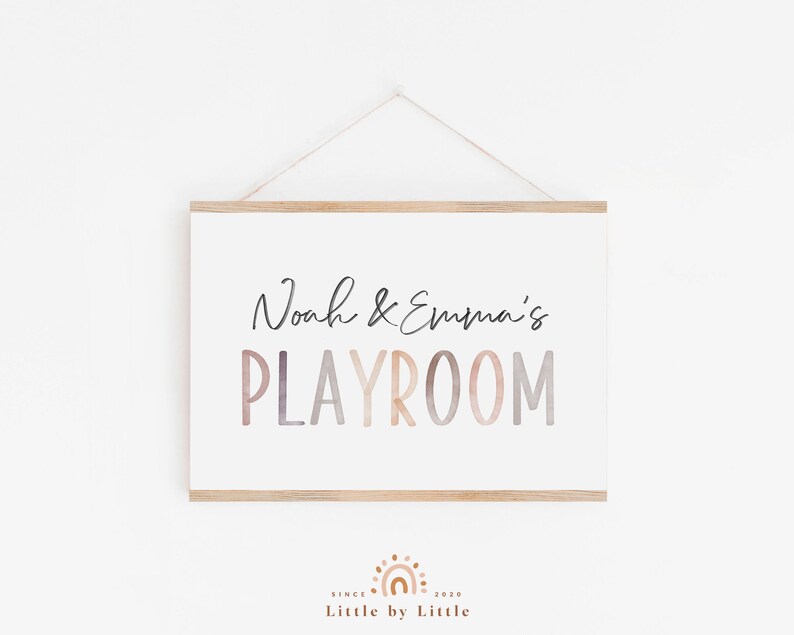 May include: A white sign with a wooden frame hangs on a white wall. The sign says "Noah & Emma's PLAYROOM" in a colorful, watercolor-style font.