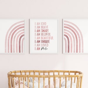 May include: Three framed prints featuring pink watercolour rainbows. The centre print displays the text "I am kind, I am brave, I am smart, I am helpful, I am beautiful, I am unique, I am loved, I am Mila".