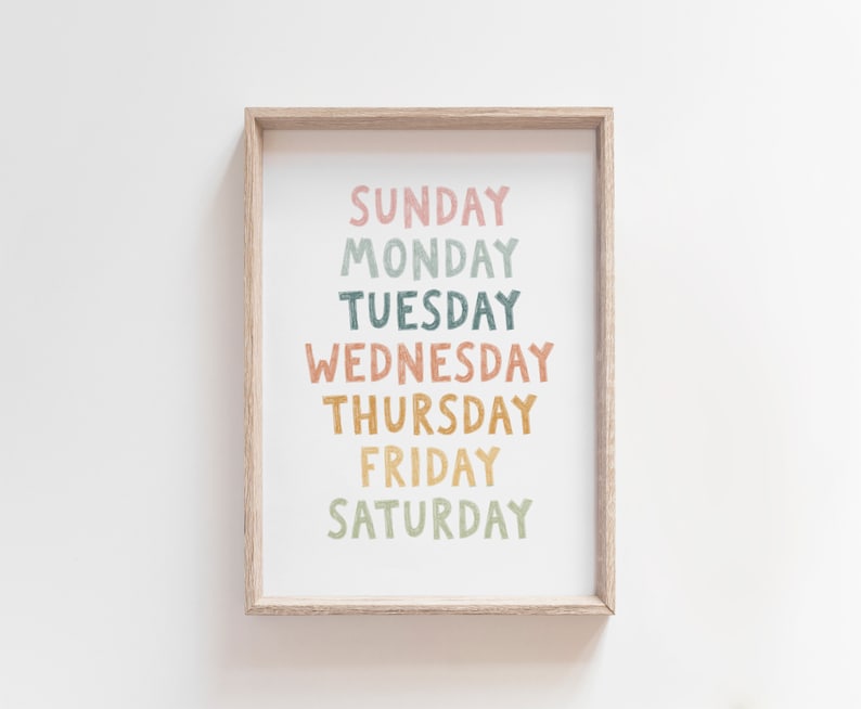 May include: A framed print with the days of the week written in a colorful, hand-drawn style. The words are arranged vertically, with "Sunday" at the top and "Saturday" at the bottom. The colors used are pink, green, blue, orange, and yellow.