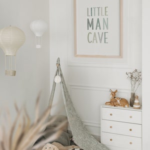 May include: A white dresser with three drawers and wooden knobs. A teepee tent with a white pom-pom on top is in the background. A framed print with the text "LITTLE MAN CAVE" is on the wall. Two small deer figurines are on top of the dresser.