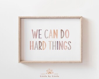 May include: A framed print with the text "WE CAN DO HARD THINGS" in a watercolor style with shades of pink, purple, and brown. The print is in a light wood frame and has a white background.