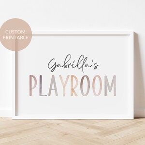 May include: A white framed print with the text "Gabriella's Playroom" in a watercolor-style font with pink, orange, and purple hues.