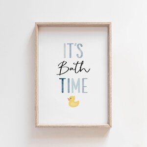 May include: A framed print with the text "It's Bath Time" in blue and black lettering. A yellow rubber duck is pictured below the text.