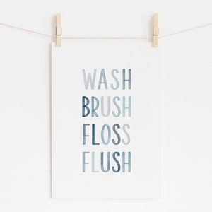 May include: A white print with the words "WASH", "BRUSH", "FLOSS", and "FLUSH" in a blue watercolor gradient. The print is hanging on a white wall with two wooden clothespins.