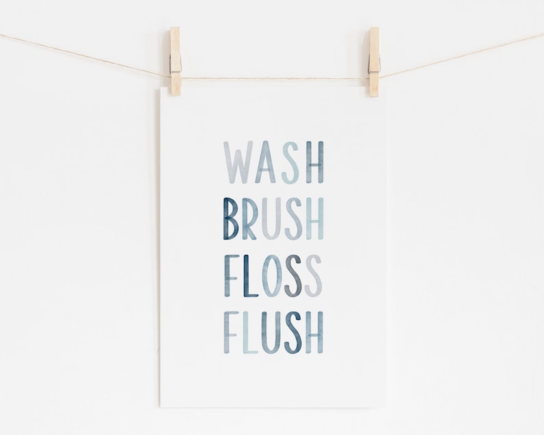 May include: A white print with the words "WASH", "BRUSH", "FLOSS", and "FLUSH" in a blue watercolor gradient. The print is hanging on a white wall with two wooden clothespins.
