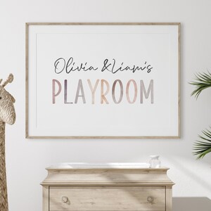 May include: A framed print with the text "Olivia & Liam's Playroom" in a watercolor-style font with a gradient of pink, orange, and purple colors.