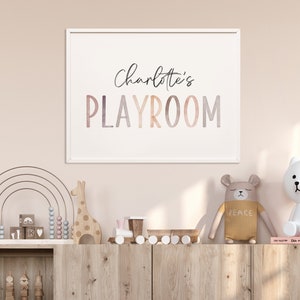 May include: A white framed print with the text "Charlotte's Playroom" in a colorful watercolor font. The print is hanging on a light pink wall above a wooden shelf with a rainbow abacus, wooden giraffe, and other toys.