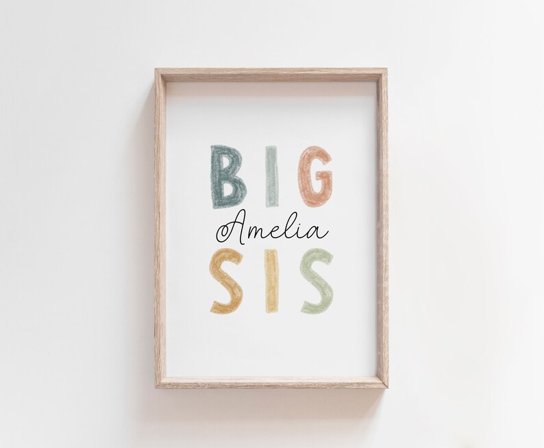 May include: A framed print with the text "BIG SIS" in colorful, hand-drawn letters. The name "Amelia" is written in cursive below the letters.