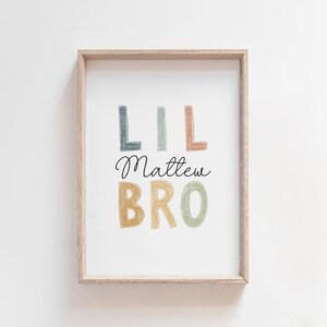 May include: A framed print with the text "Lil Matthew Bro" in colorful, hand-drawn letters. The letters are in shades of blue, green, yellow, and orange.