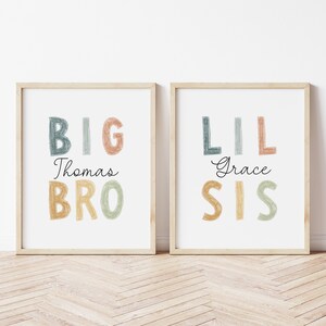 May include: Two framed prints with colorful text. The left print says "BIG Thomas BRO" in a rainbow color scheme. The right print says "LIL Grace SIS" in a rainbow color scheme.