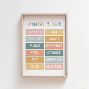 May include: A framed printable wall art poster with a colorful design featuring the months of the year in a grid layout. The months are written in a handwritten font and are arranged in two columns. The background is white.