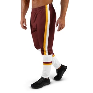 May include: Maroon joggers featuring a vertical yellow and white stripe running down the side of the leg. The lower portion of the joggers is white with a horizontal maroon and yellow stripe detail above the ankle, finished with a waistband.
