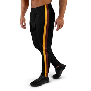 May include: Black joggers featuring a vertical side stripe with a yellow band adjacent to a maroon band. The trousers have an elastic waistband and tapered cuffs at the ankles, providing a streamlined fit for athletic or casual wear.