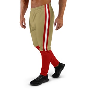 Könnte beinhalten: Goldene und rote Sporthose mit weißen Streifen an den Seiten. Die Hose hat einen Kordelzugbund und eine lockere Passform.