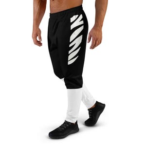 Könnte beinhalten: Schwarz-weiße Sporthose. Die Hose ist von der Taille bis zu den Knien schwarz, mit einem weißen Streifendesign am linken Bein. Die Unterschenkel sind weiß. Die Hose wird mit schwarzen Sportschuhen getragen.