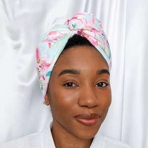 Pode incluir: Uma mulher de pele escura está usando um roupão branco e um turbante de cabelo com estampa floral. O turbante está amarrado no topo de sua cabeça.
