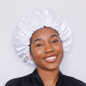 May include: A woman wearing a white satin sleep cap and a black satin robe. She is smiling at the camera.